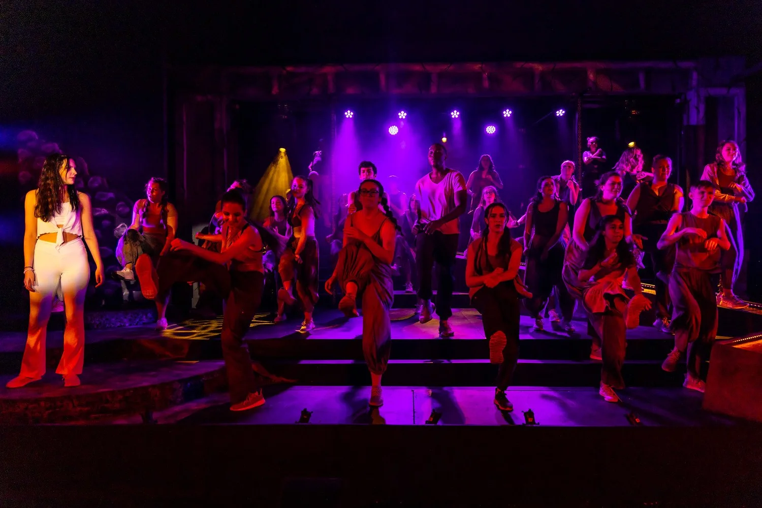 A large youth ensemble performs under purple and red stage lights