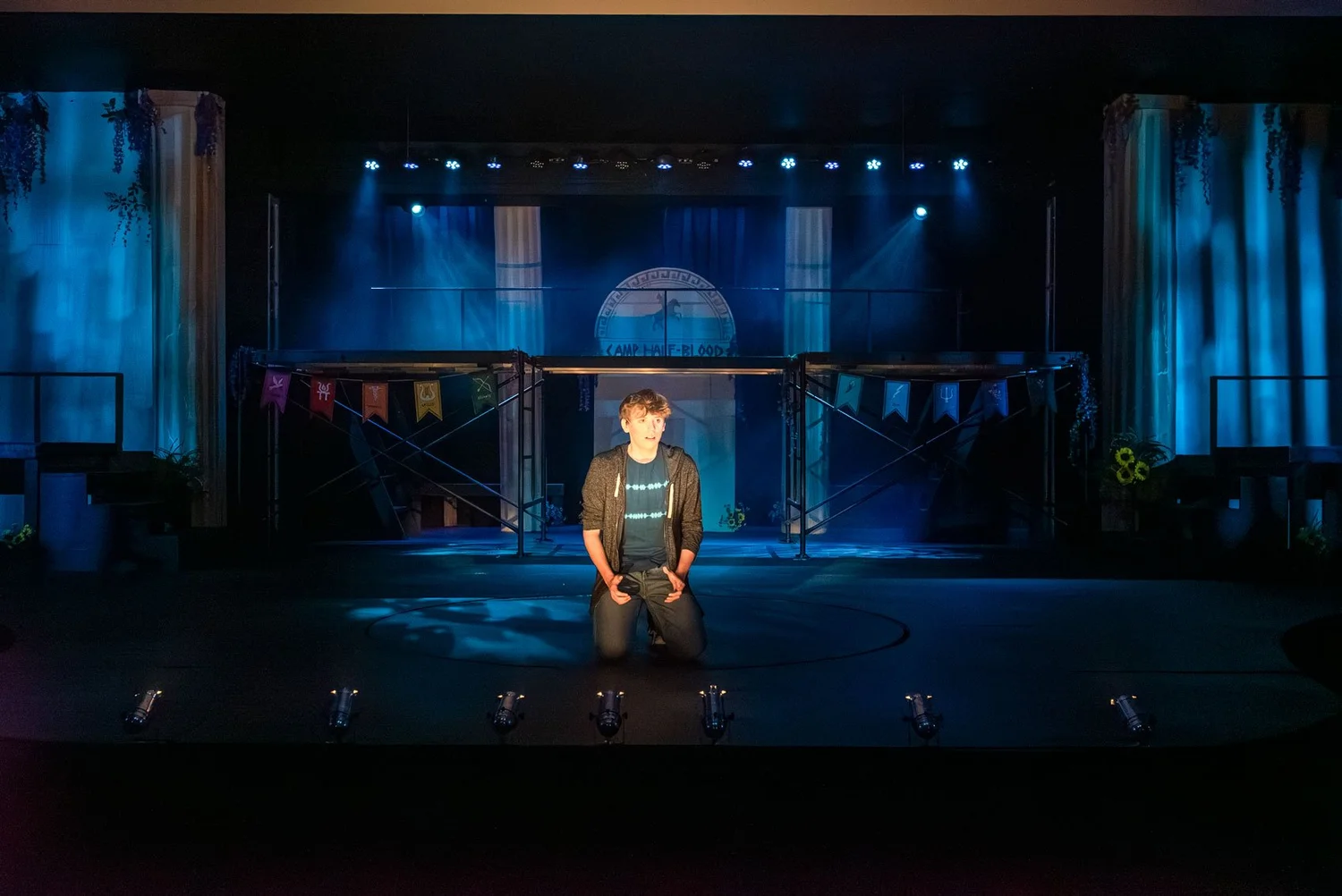 A solo performer kneels beneath blue stage lighting